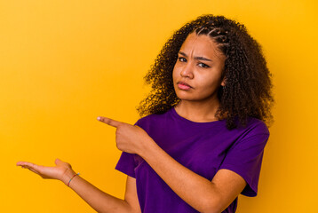 Young african american woman isolated on yellow background excited holding a copy space on palm.