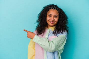 Young african american woman isolated on blue background smiling and pointing aside, showing something at blank space.