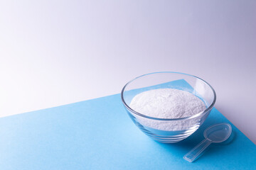Glass plate with collagen powder and measuring spoon on a blue background.