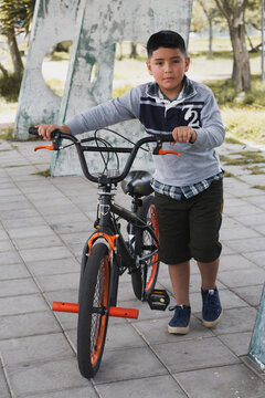 A hispanic smiling cute  child standing at the park bnext to his bicycle looking at the camera