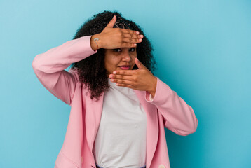 Young african american woman isolated on blue background blink at the camera through fingers, embarrassed covering face.