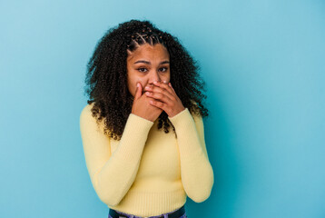 Young african american woman isolated on blue background covering mouth with hands looking worried.