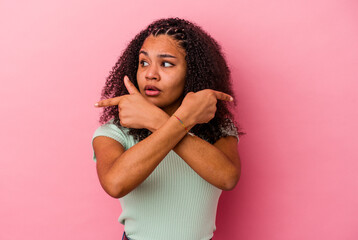 Young african american woman isolated on pink background points sideways, is trying to choose between two options.