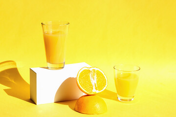 Fresh and juicy orange juice in glasses on trendy white catwalks with hard shadows on a yellow background. Healthy food and drink concept. Copy space