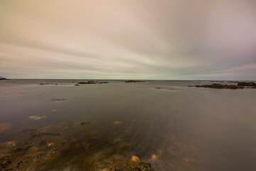A horizontal photo with a long exposure of the sea horizon, several rocks protruding in the distance.