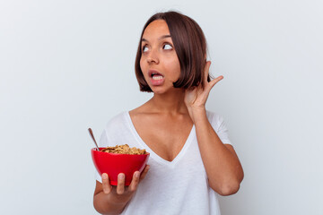 Young mixed race woman eating cereals isolated on white background trying to listening a gossip.