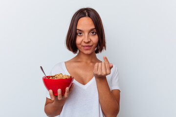 Young mixed race woman eating cereals isolated on white background pointing with finger at you as if inviting come closer.