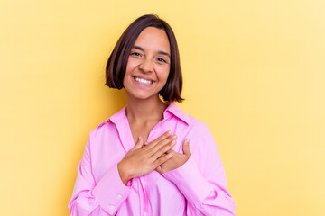 Young mixed race woman isolated on yellow background has friendly expression, pressing palm to chest. Love concept.