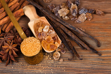 Vanilla beans, brown sugar in a spoon and scoop with star anise and cinnamon sticks on a wooden background. Top view. Sweet spices concept.