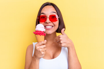 Young mixed race woman holding an ice cream isolated on yellow background