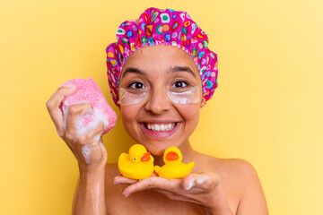 Young mixed race woman with shower cap holding a sponge and rubber ducks isolated on yellow background