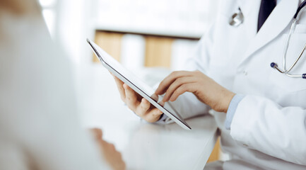 Unknown male doctor and patient woman discussing current health examination while sitting in clinic and using tablet computer. Perfect medical service in hospital. Medicine and healthcare concept
