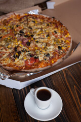 A mug of aromatic coffee and delicious homemade pizza with corn, meat, tomatoes, mushrooms and cheese. Pizza up close. 