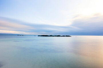 Long exposure photograph, clear blue water, a small island can be seen in the distance.