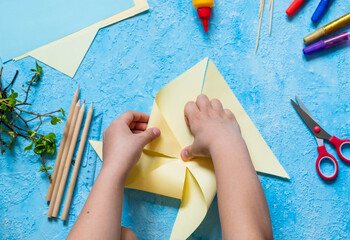 Step-by-step making of a paper weather vane by a child on a blue concrete background. Children's...