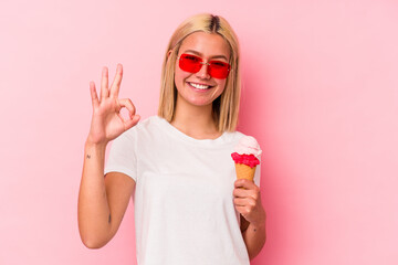 Young venezuelan woman eating an ice cream isolated on pink background cheerful and confident showing ok gesture.