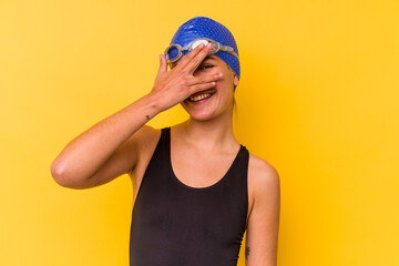 Young swimmer venezuelan woman isolated on yellow background blink at the camera through fingers, embarrassed covering face.