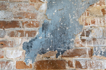 An old wall of red brick with remnants of plaster and cracked paint
