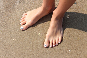 Pedicure on a background of sea sand. Selective focus. Beautiful legs with manicure on the sea sand