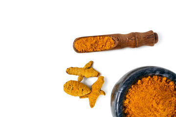 Turmeric powder spice heap in a black stone bowl with turmeric roots and bamboo scoop isolated on a white background. Top view.