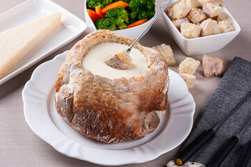 Creamy cheese fondue inside Italian bread. Fork dipping bread in cream cheese