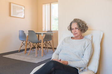 Pensive senior woman sitting on chair at home (selective focus)