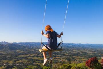 Red haired teenage girl swinging on a swing in Mountains