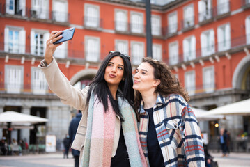 two tourist girls take a selfie in the central square of the city. Plaza Mayor, Madrid