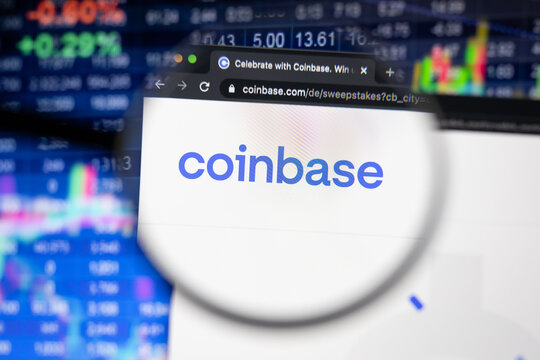 Coinbase company logo on a website with blurry stock market developments in the background, seen on a computer screen through a magnifying glass