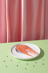 Fresh fish salmon on a geometric white plate with pink and green backround. Creative conceptual still life, minimalism, trending shadow, creative food
