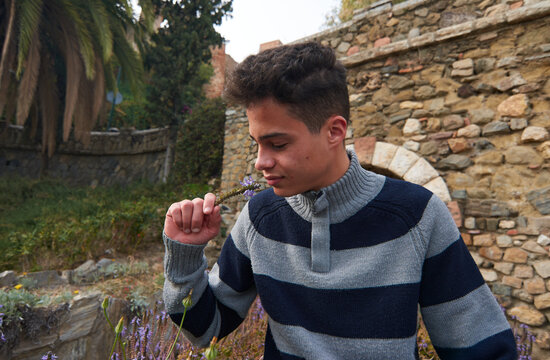 A Handsome Young Hispanic Guy Wearing A Sweater Smelling A Flower Outdoors