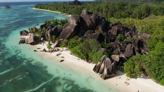 Bright sunny aerial shot of Anse source D&rsquo;Argent beach. Vacation paradise island La Digue, Seychelles. Drone shot of tourist wading in turquoise blue ocean water and white sand with coconut palm trees