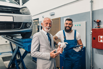 Car mechanic talking with senior business man costumer during periodic car condition check. Technical inspection.