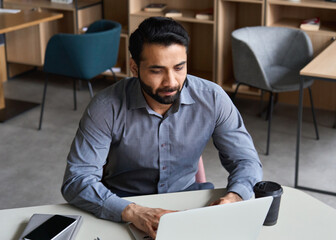 Serious indian businessman remotely working at home watching online learning training webinar for...