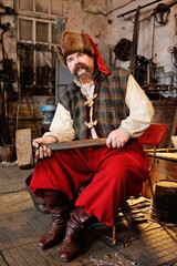 portrait of a blacksmith with a beautiful thick mustache with a huge hammer in the hands on the background of the forge.