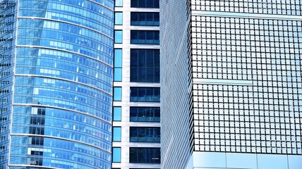 Abstract closeup of the glass-clad facade of a modern building covered in reflective plate glass. Architecture abstract background. Glass wall and facade detail. Velvia graphic filter.