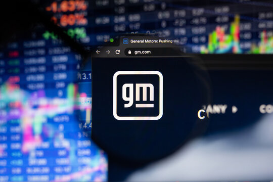 General Motors company logo on a website with blurry stock market developments in the background, seen on a computer screen through a magnifying glass