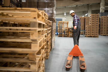 Skilled warehouse employee operating manual forklift and working in factory storage room.
