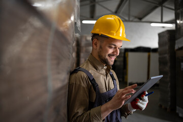 Portrait of caucasian smiling warehouse worker standing by palettes and checking inventory on...