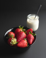 Strawberries and a cup of yogurt on a dark background