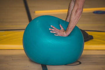 Man is seen balancing on a plastic ball with his hands, trying to stand straight. Detail on hands.