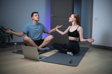Fototapeta premium The newlyweds home room for yoga classes, they meditate on the floor under a video with relaxing music from a laptop