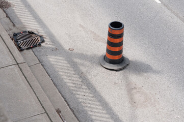 stripped orange and black construction pylon near the edge of a road, featuring a sewer grate (or...
