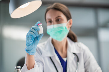 A young female lab technician wearing a medical mask shows off a coronavirus vaccine in her lab at the hospital