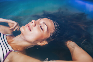 Beautiful woman floating in tank filled with dense salt water used in meditation, therapy, and alternative medicine.