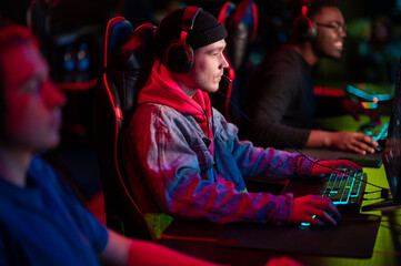 Fototapeta na wymiar Training bootcamp for professional esports players. Young cyber-athletes play an online shooter game. Glowing keyboard, neon light.