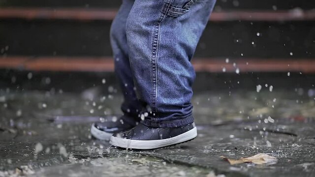Child jumping into puddle in slow-motion. Toddler jumps into water