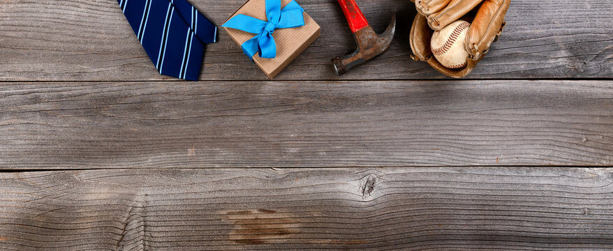 Fathers day top border concept with blue dress tie, hammer, baseball items and a gift box on rustic wooden background