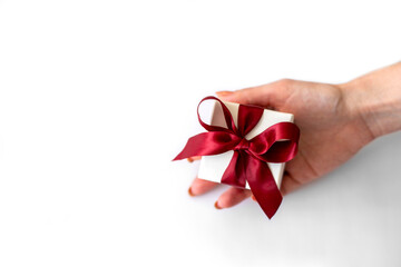 Female hand holds white box with red bow on white background. Gift box in female hand
