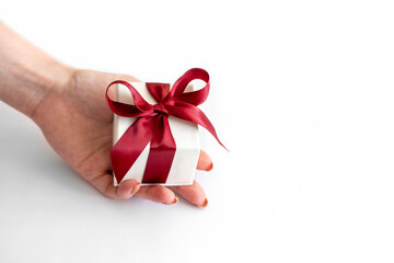 White box with red bow lies in awoman's hand on white background. Gift box in female hand